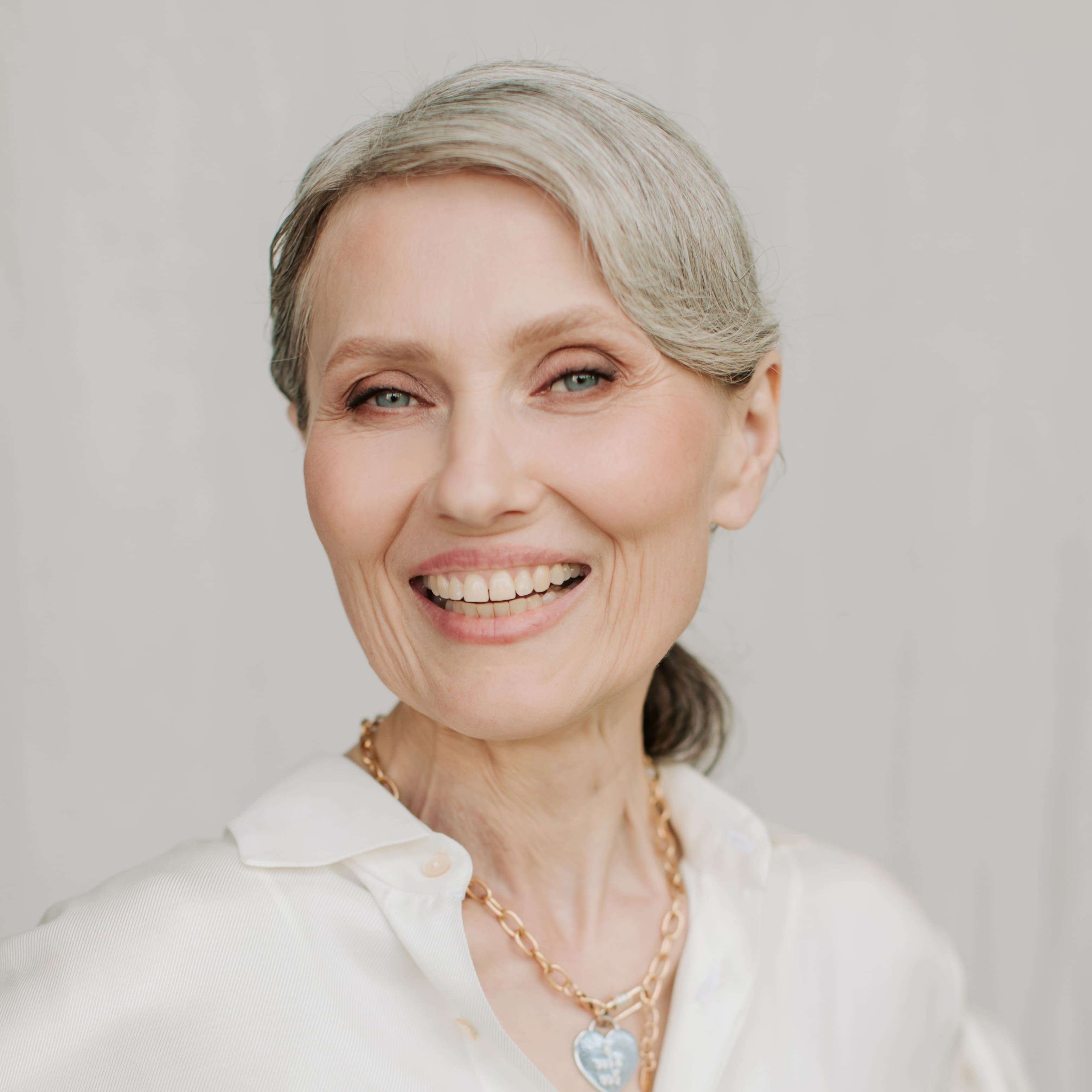 Portrait d’une femme élégante aux cheveux gris et à la peau éclatante, souriant avec confiance — illustration de la beauté naturelle et des bienfaits anti-âge de l’huile de graines de figue de barbarie sauvage bio.